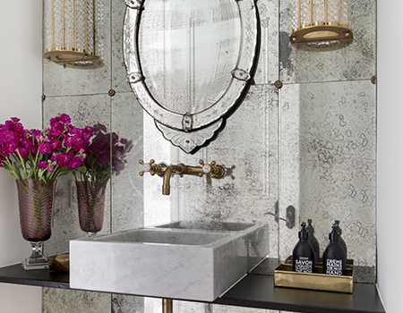 Custom powder bathroom with antiqued mirror wall and floating white square sink with brass fixtures in Houston, TX